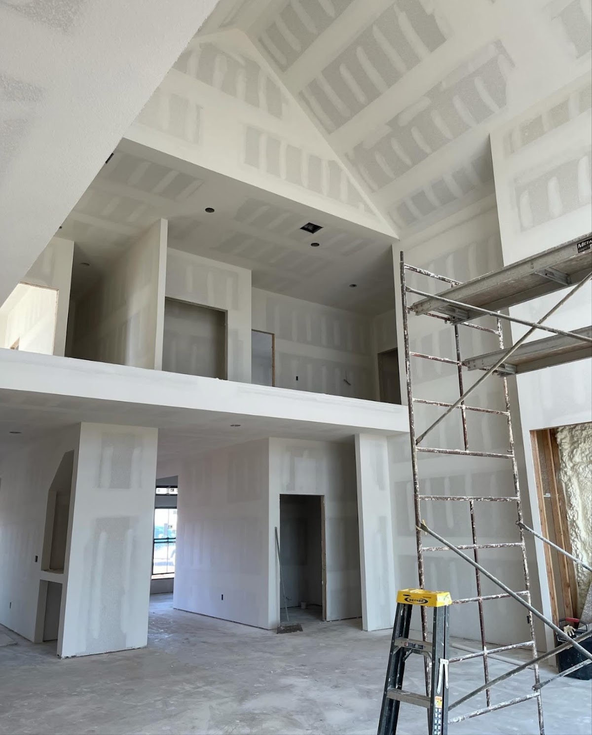 Drywall tape and mud work on a vaulted ceiling with scaffolding on site